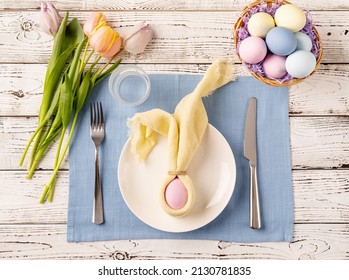 Happy Easter. Table Setting For Easter Feast. Easter Eggs, Bunny, Tulips And Cutlery Top View Flat Lay On White Rustic Background