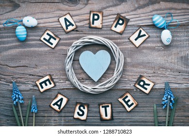 Happy Easter Text On Rustic Wood With Blue Heart In Wattle Wreath, Hyacinth Flowers And Easter Eggs