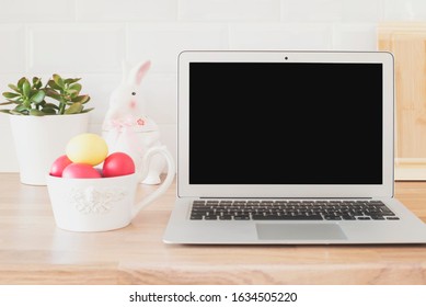 Happy Easter! Workspace With Laptop, Easter Eggs, Rabbit, Succulent On The Kitchen Counter, Close Up. Kitchenware In Modern Kitchen Interior. White Tiles Background