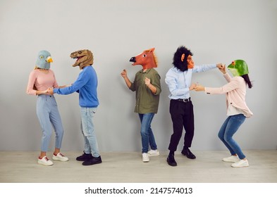 Happy Eccentric Young People With Heads Of Various Animals Dance And Have Fun Together. Five Casual People In Funny Bizarre Rubber Carnival Masks. Absurd Concept Of Masquerade Funny Holidays.