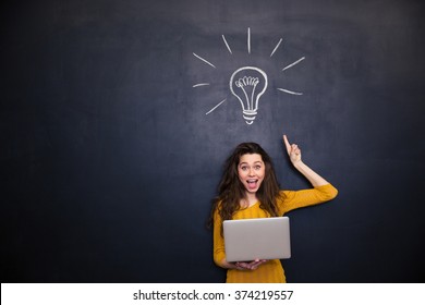 Happy elated young woman holding laptop and having an idea over blackboard background - Powered by Shutterstock