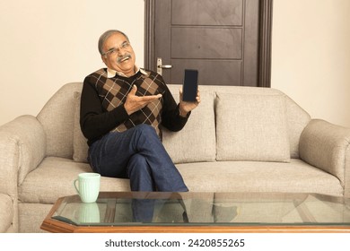 Happy elder man talking on smart phone while  sitting on cozy couch at home. wearing sweater. Old male modern  communicating having cellphone conversation indoor.  - Powered by Shutterstock