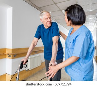 Happy elder man with walker talking to nurse in hospital corridor.