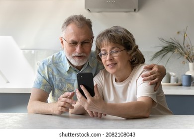 Happy elder married couple using mobile hone for video call, talking to family together, watching online content, reading message, sing internet banking app, chatting. Distant communication concept - Powered by Shutterstock