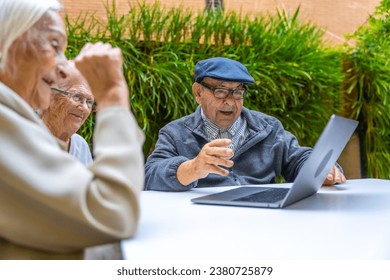 Happy elder people using laptop sitting on a garden in a nursing home - Powered by Shutterstock