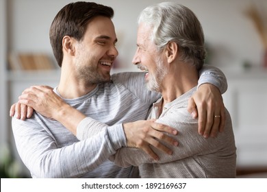 Happy Elderly 70s Caucasian Father Hug Embrace Adult Son Enjoy Family Reunion On Weekend At Home. Smiling Caring Millennial Grownup Man Show Love Feel Thankful To Mature Dad. Gratitude Concept.