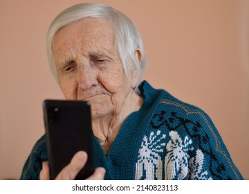 Happy elderly 90-year-old woman wearing a green jacet smiles using a smartphone, video call conversation with family.