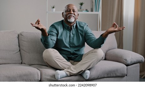 Happy elderly african american man sit on sofa in lotus position with folded fingers grandpa is meditating finds harmony relieves stress positive calm pensioner relaxing at home improve self-conscious - Powered by Shutterstock