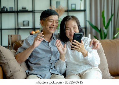 Happy Elderly Asian Couple Doing Facetime Video Calling With A Smartphone At Home Using The Zoom App, Online Meetings, Social Media, New Normal Concepts