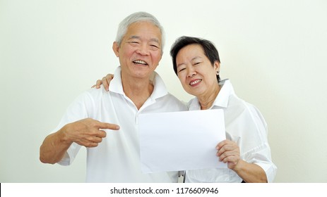 Happy elderly Asian couple hold copy space white sign - Powered by Shutterstock