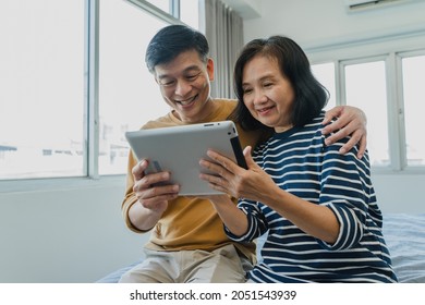 Happy elderly Asian couple smiling and looking at the same tablet hugged on the bed, at home concept - retired man and woman using technology - lockdown and quarantine lifestyle - Powered by Shutterstock