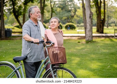 Happy Elderly Asian Couple Walking Talking Together With Bicycles In The Park. Holiday Activities For Retired Couples.