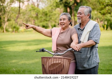 Happy Elderly Asian Couple Walking Talking Together With Bicycles In The Park. Holiday Activities For Retired Couples.