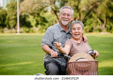 Happy Elderly Asian Couple Walking Talking Together With Bicycles In The Park. Holiday Activities For Retired Couples.