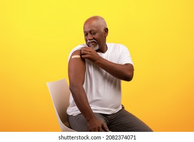 Happy Elderly Black Man Showing Band Aid On Shoulder After Coronavirus Vaccination Over Orange Studio Background. Senior Male Patient With Plaster Smiling At Camera After Getting Covid-19 Vaccine