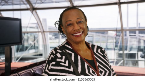 Happy elderly black woman waits at the airport gate smiling at camera
