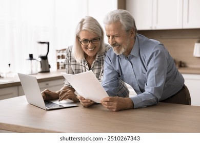 Happy elderly couple hold documents papers, read bank notice with positive news, make payment on internet banking services. Enough of money to pay bills, repayment, pension raise and good fixed income - Powered by Shutterstock