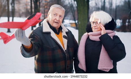 Happy Elderly Couple Playing With Airplane Toy In The Park. Winter Holiday Plans. High Quality Photo