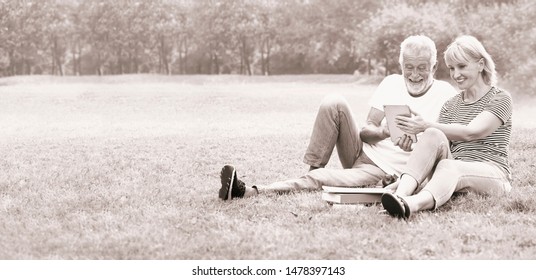 Happy Elderly Couple Relaxing In The Park And Play IPad.                            