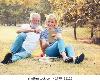 Happy Elderly Couple Relaxing In The Park And Play IPad.