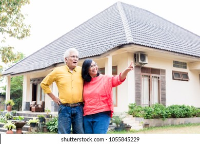 Happy elderly couple showing thumbs up in front of their new residential property - Shutterstock ID 1055845229