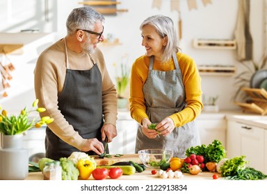 Happy elderly couple smiling husband and wife in aprons prepare salad together at kitchen table, chopping variety of colorful vegetables, trying to maintain healthy lifestyle eating vegetarian food - Powered by Shutterstock