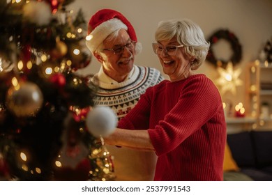 Happy elderly couple smiling while decorating a Christmas tree at home during holidays - Powered by Shutterstock