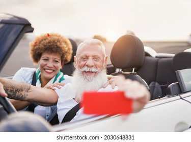 Happy Elderly Couple Taking A Selfie With Mobile Phone Inside Convertible Car On A Road Trip