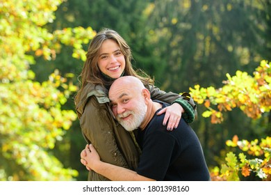 Happy Elderly Father And Daughter Enjoying Tender Autumn Moment, Smiling. Grown Up Daughter Hugging Mature Man From Back, Two Generations Having Fun Together