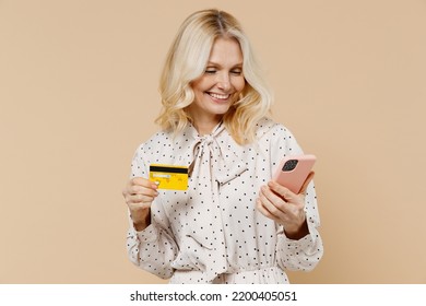 Happy Elderly Gray-haired Blonde Woman Lady 50s Years Old Wears Pink Dress Using Mobile Cell Phone Hold Credit Bank Card Doing Online Shopping Isolated On Plain Pastel Beige Background Studio Portrait