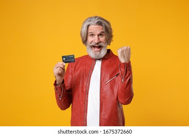 Happy elderly gray-haired mustache bearded man in red leather jacket isolated on yellow orange background. People lifestyle concept. Mock up copy space. Hold credit bank card, doing winner gesture - Shutterstock ID 1675372660