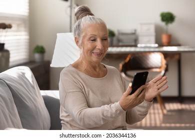 Happy elderly grey haired lady using smartphone at home, making video call, talking to family, relatives online. Senior patient consulting doctor at virtual meeting on mobile phone, smiling at screen