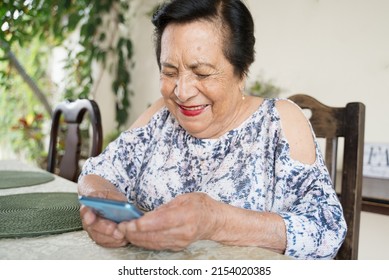 Happy Elderly Hispanic Woman Using Smartphone. Old Latina Woman Texting With Cellphone.  