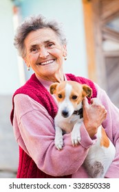 Happy elderly lady holding her little pet dog outdoors in the garden.