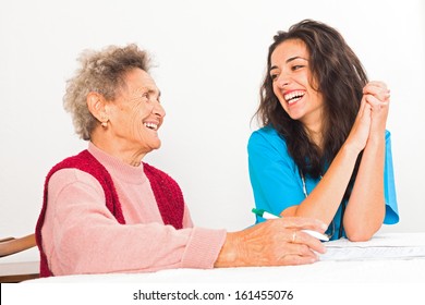 Happy Elderly Lady Laughing With Kind Nurse Carer Working In Homecare.