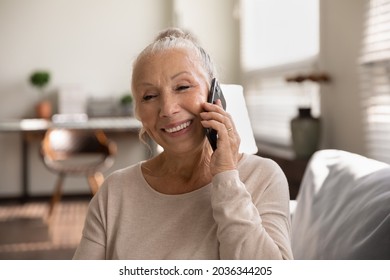Happy elderly lady talking on cellphone, making call from home, speaking to family on mobile phone with toothy smile. Senior 70s woman consulting doctor on cellphone, chatting to friend, laughing