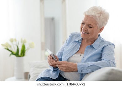 Happy Elderly Lady Using Mobile Phone While Relaxing On Couch At Home, Browsing Social Networks Or Online Banking App, Free Space