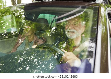 Happy elderly man driving while traveling with woman in car seen through windshield during vacation
