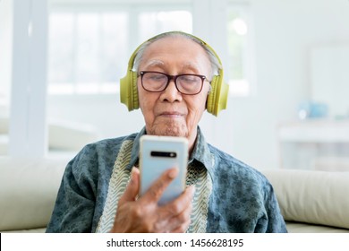 Happy elderly man enjoying music with a smartphone and headphones on the sofa at home