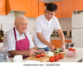 Happy Elderly Man And His Grandson Making Dinner Together In Kitchen