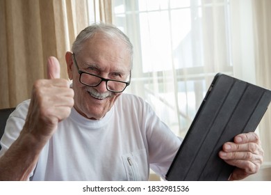 Happy Elderly Man At Home With Laptop. A Gray-haired Old Man With Glasses Is Happy And Gestures That Everything Is OK. The Concept Of Communication Between Older People