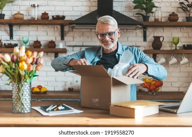 Happy Elderly Man Open A Parcel, Delivery Of Online Shopping To Home. A Satisfied Senior Customer.