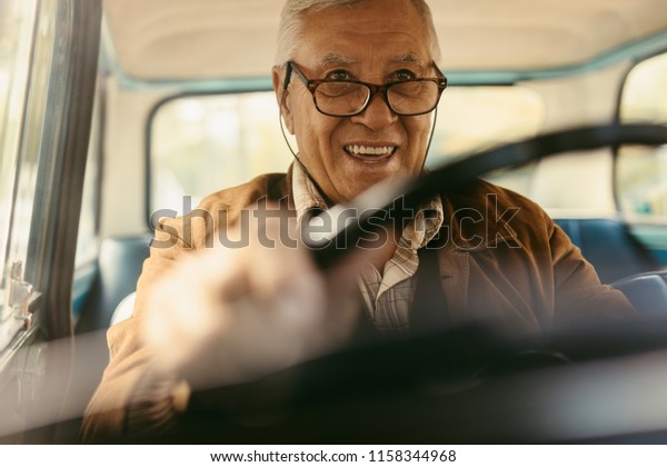 Happy elderly man wearing\
eyeglasses driving a car. Happy old man enjoying driving his\
car.