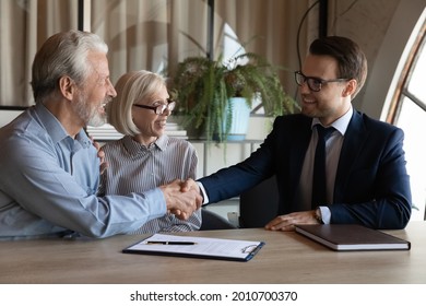 Happy Elderly Married Couple Shaking Hands With Realtor, Agent, Notary, Lawyer. Mature Man And Woman Buying House, Medical Insurance, Consulting Professional, Giving Handshake Over Documents