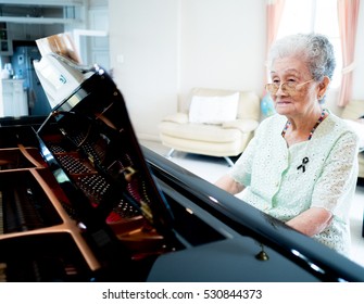 Happy elderly pianist lady woman is playing piano at home. Activity for retirement woman relaxed by learning to play piano.