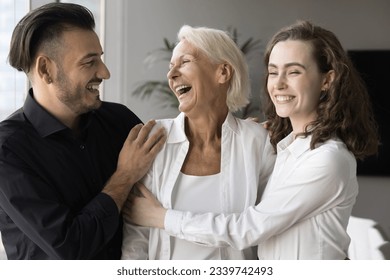Happy elderly retired mom and adult son and daughter hugging with love, affection, talking, chatting, laughing, standing close, enjoying family relationships, celebrating mothers day