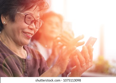 Happy Elderly Senior People Society Lifestyle Concept. Ageing Asia Women Using Smartphone Share Social Media Together In Wellbeing County Home.