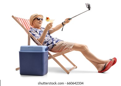 Happy elderly tourist with a cocktail sitting in a sun lounger and taking a selfie isolated on white background - Powered by Shutterstock