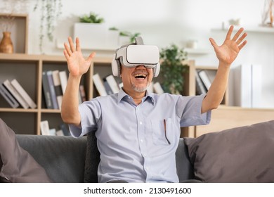 Happy elderly using VR or Virtual Reality glasses headset pointing objects or talking in community with friends in metaverse world.Excited and surprise senior asian man having fun with goggle using VR - Powered by Shutterstock