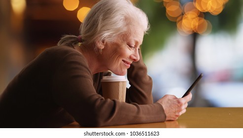 Happy elderly white woman using mobile device sitting outside at coffee shop
